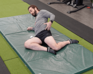 Leaning back onto his right elbow, Dr. John has both legs fallen to the right side.  he is stretching the top hip while extending through his hips for his 5 minute mobility routine
